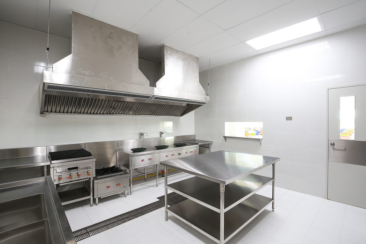 A commercial kitchen with stainless steel benches, cooking equipment and extraction hoods