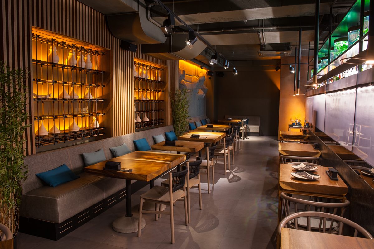 A restaurant dining room with timber tables, banquette seating and a back-lit wall of bottles