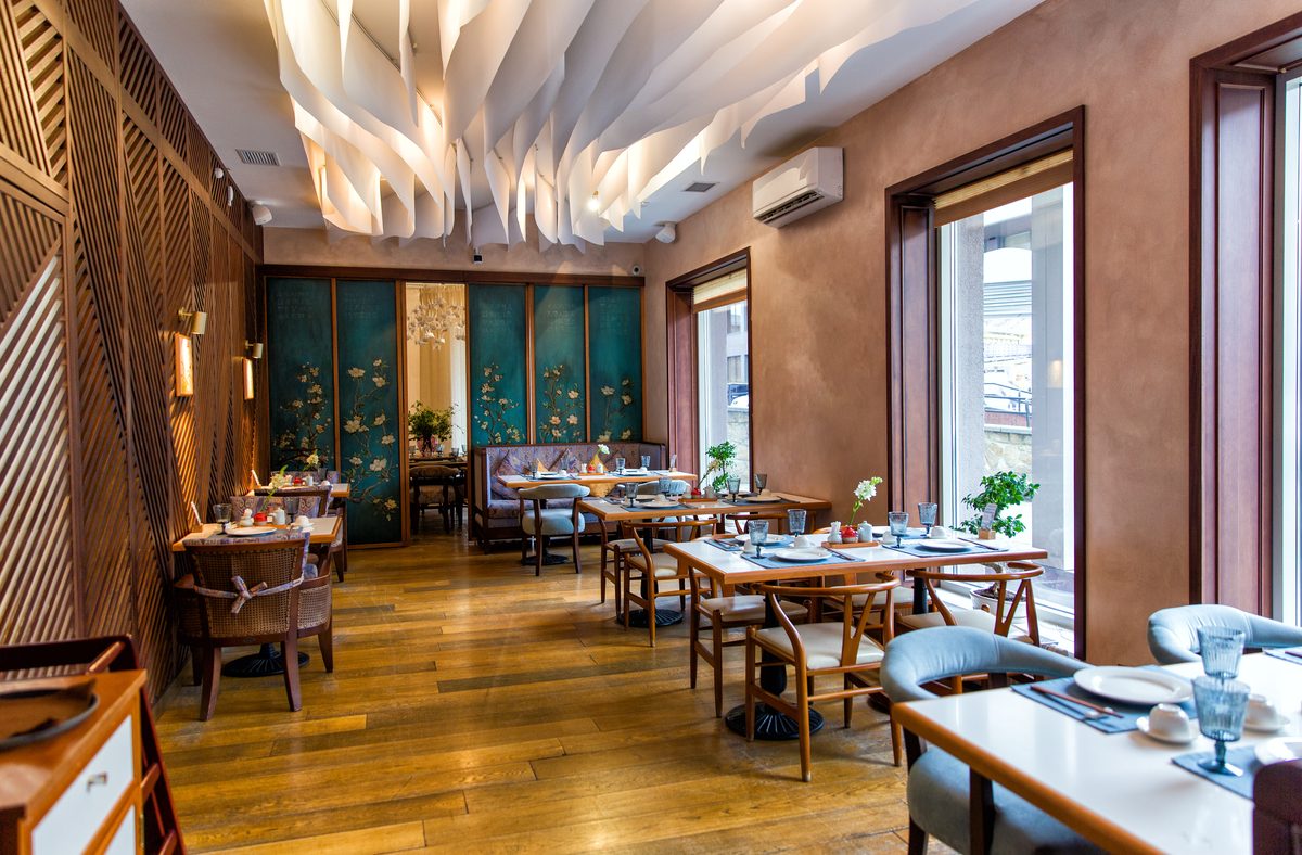 A restaurant with set tables, a timber floor and a sculptural white ceiling feature above